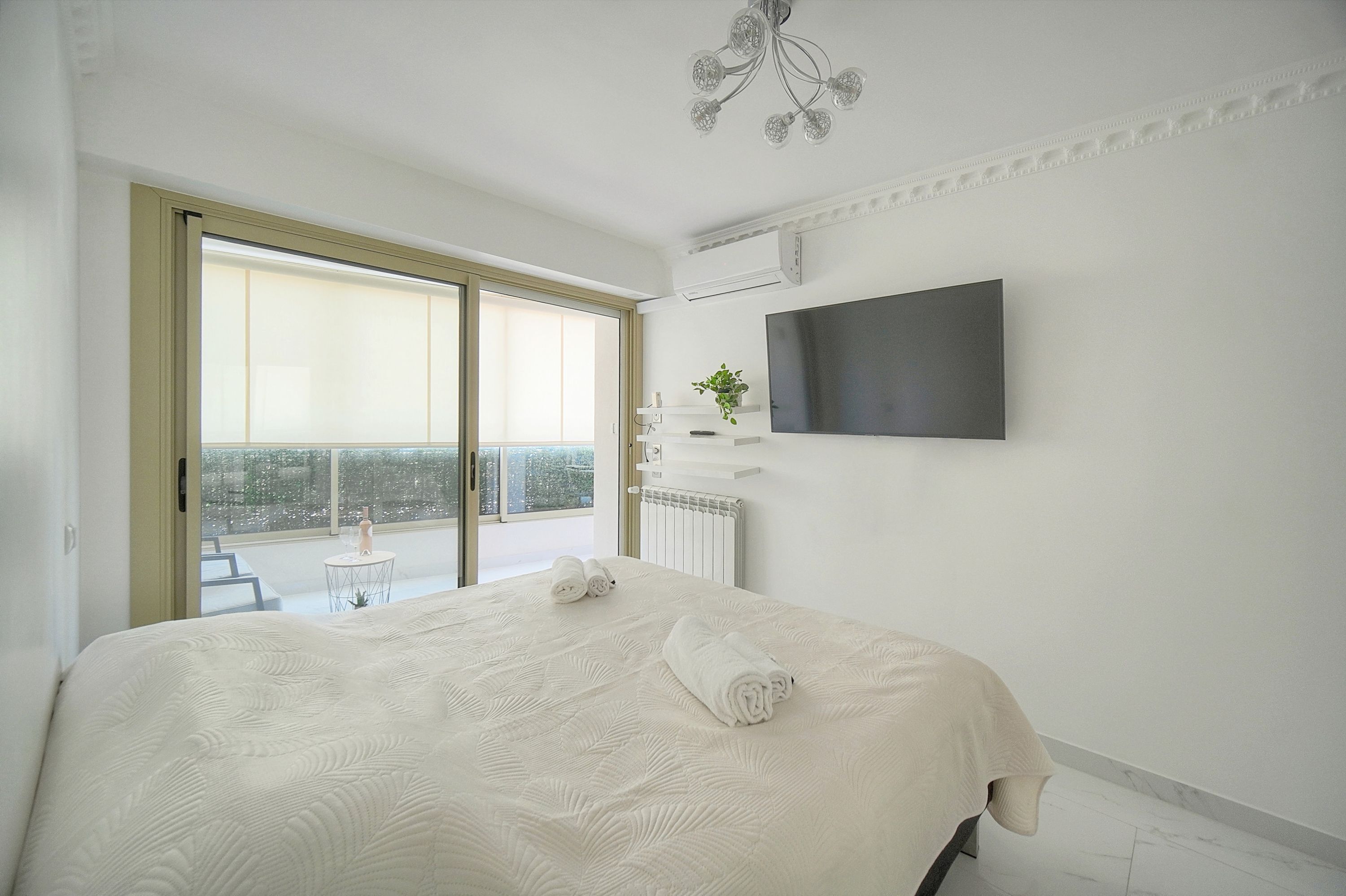 Una camera d'albergo moderna con un letto grande, una TV a schermo piatto montata a parete, un balcone con vista e un tavolino con una pianta.