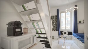 A compact, modern room with a kitchen area, a staircase with a unique design, a window with curtains, and a bed with a blue bedspread. - Charmant Studio Hypercentre A0b211 (Cannes)