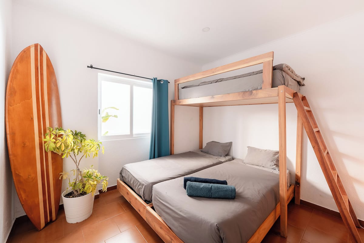 A compact room with a bunk bed, a surfboard leaning against the wall, and a potted plant.