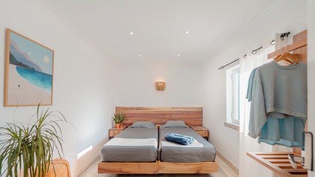 Une chambre à coucher avec un cadre de lit en bois, deux lits simples, une table de chevet, un luminaire suspendu, une étagère fixée au mur et un tableau encadré.