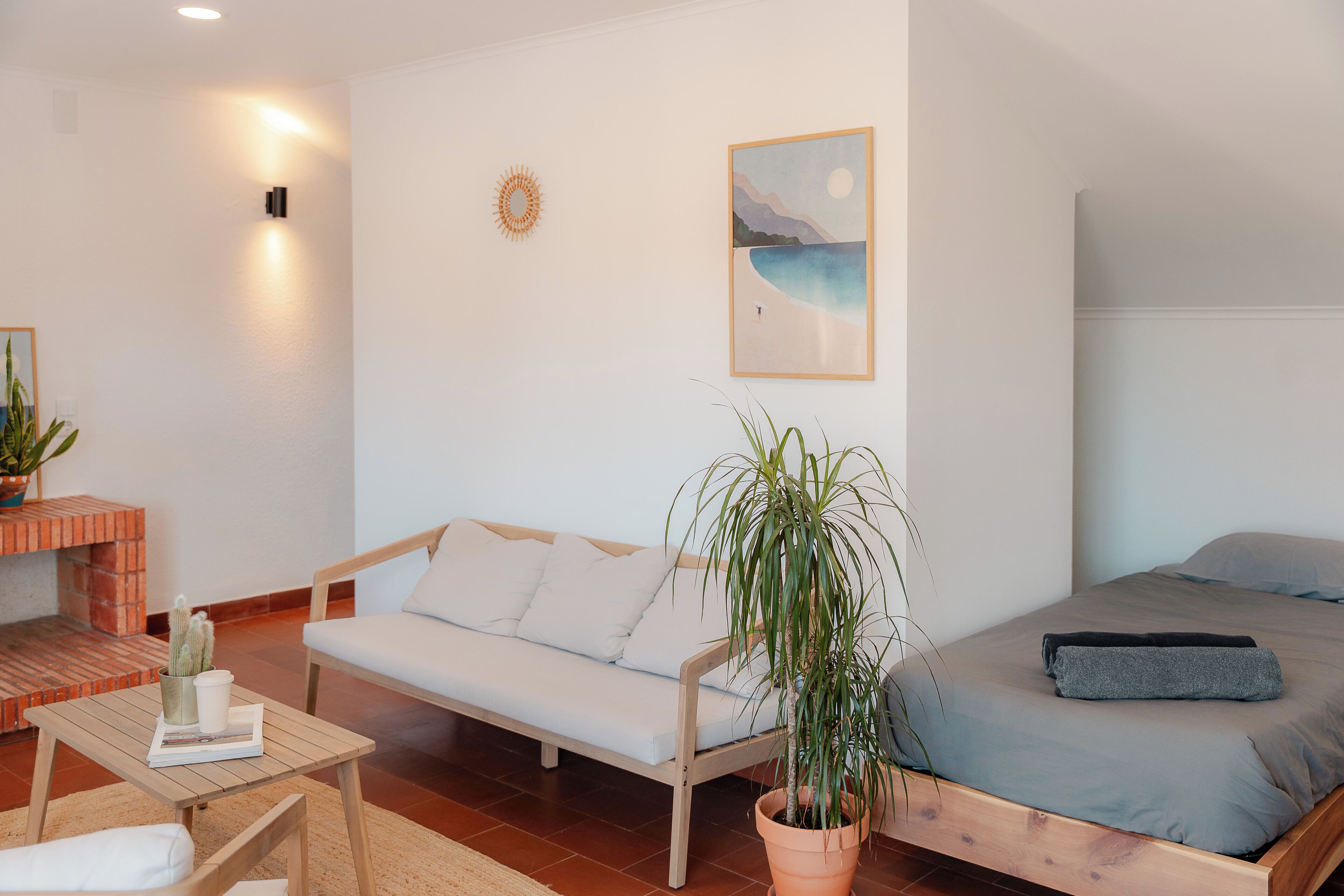 Quarto com cama, sofá, uma mesinha com uma planta e luminária na parede.