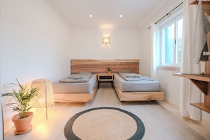 A modern bedroom with two beds, a wooden headboard, a bedside lamp, a potted plant, and a view of the outdoors.