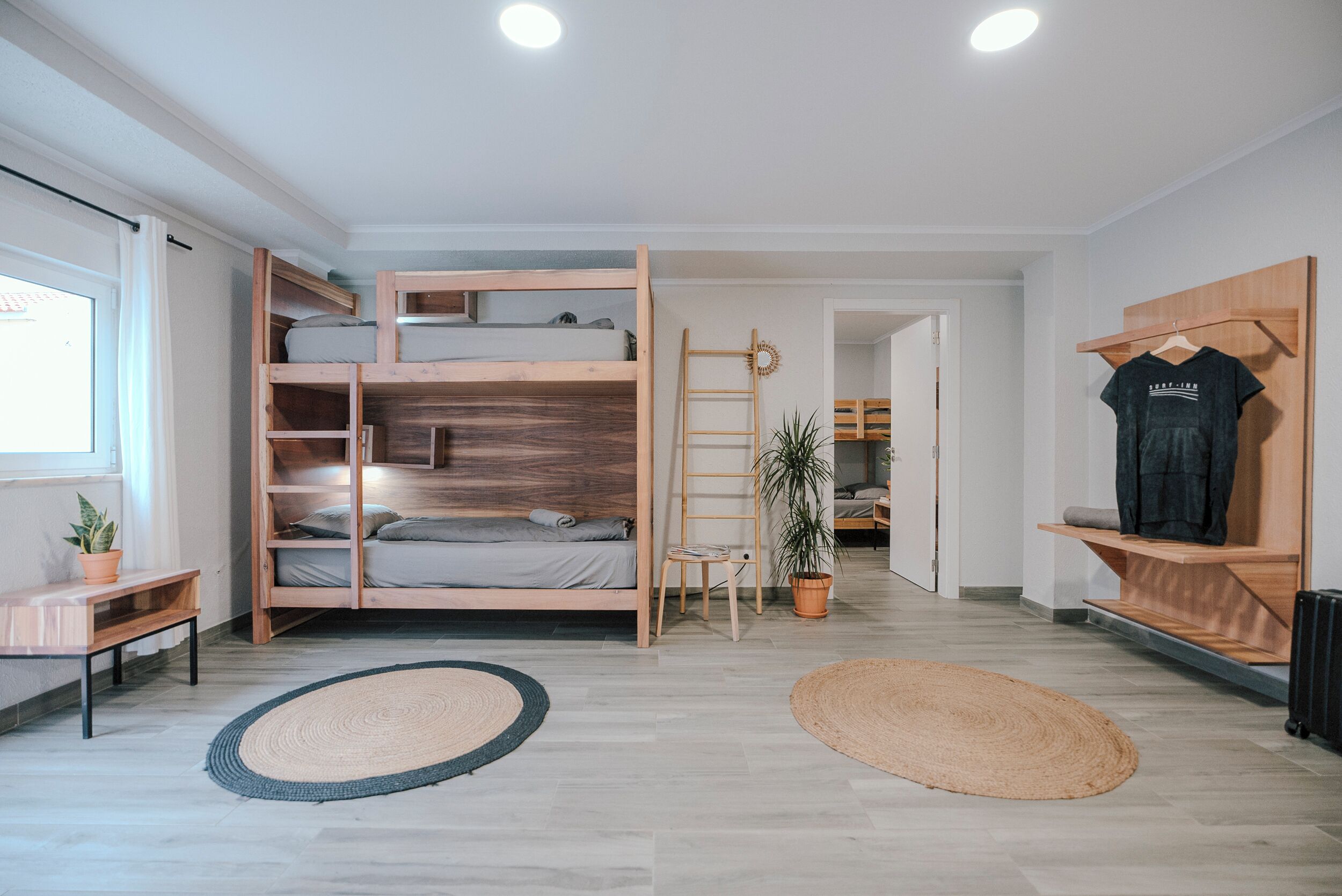 A room with a bunk bed, a desk, a chair, a potted plant, and a hanging rack with clothes.