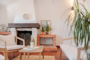 A cozy living room with a fireplace, two white sofas, a wooden coffee table, and a potted plant.