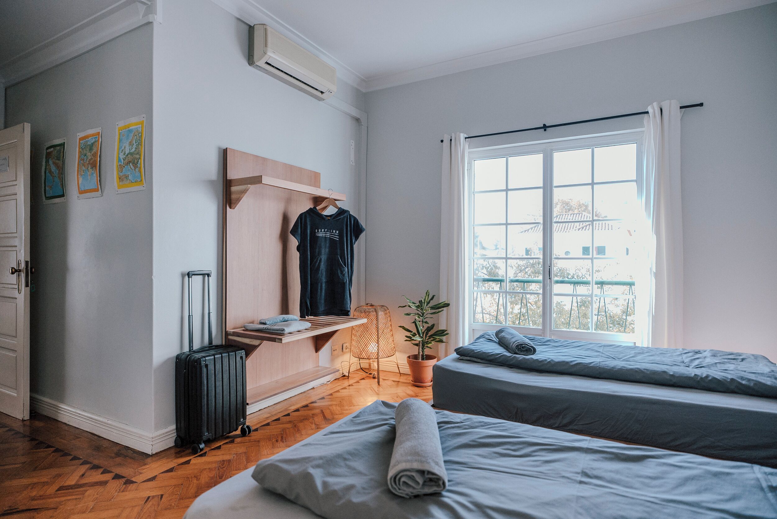 A hotel room with two beds, a suitcase, a potted plant, and a window with a view.