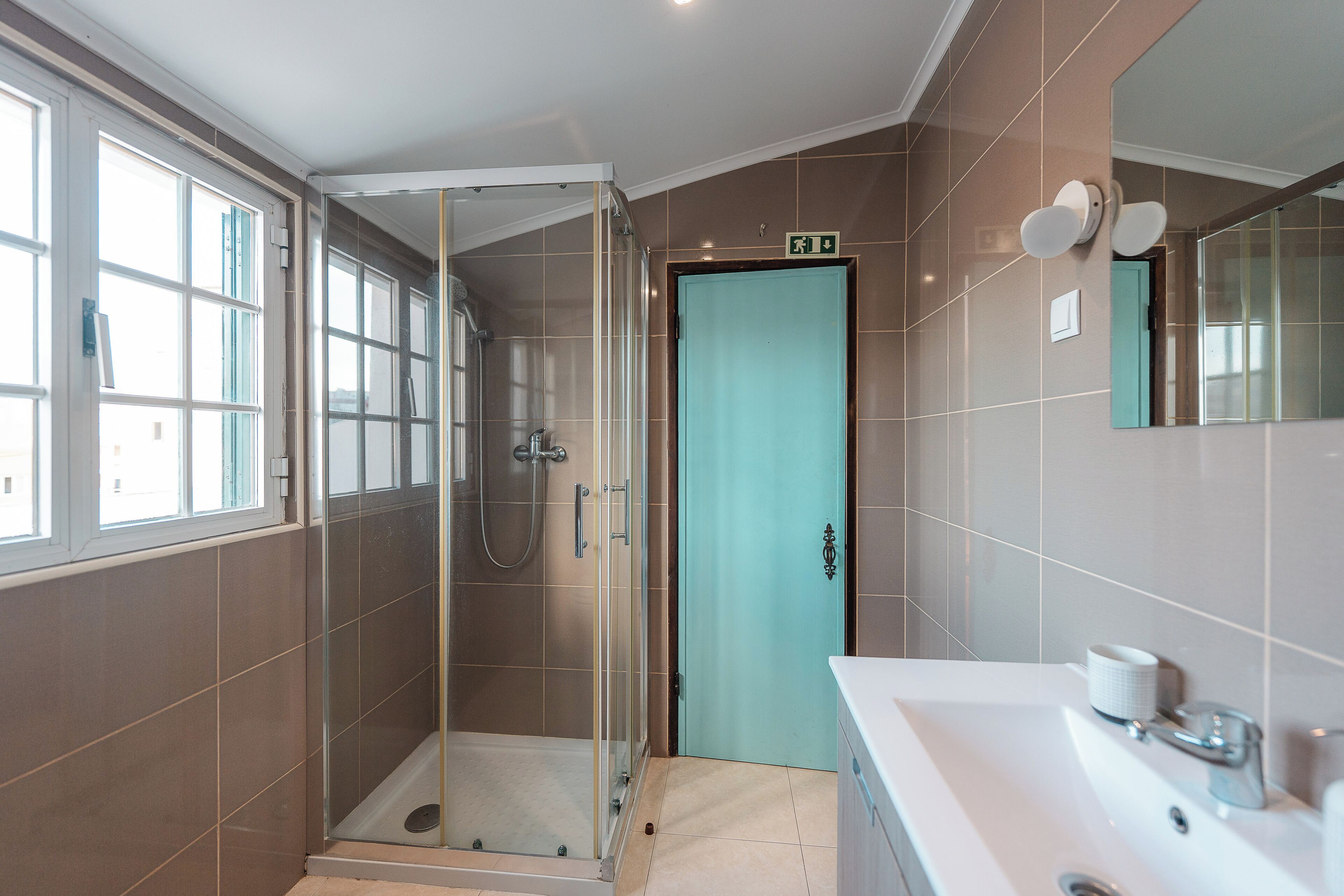 Ein modernes Badezimmer mit Duschabtrennung aus Glas, einem Waschbecken mit Spiegel und einer türkisblauen Tür.