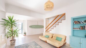 Un salon spacieux avec un canapé beige, une bibliothèque bleue, une plante en pot et un escalier.