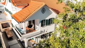 Un bâtiment à deux étages, doté d’un toit recouvert de tuiles rouges, d’un balcon avec un fauteuil en osier et d’une petite table.