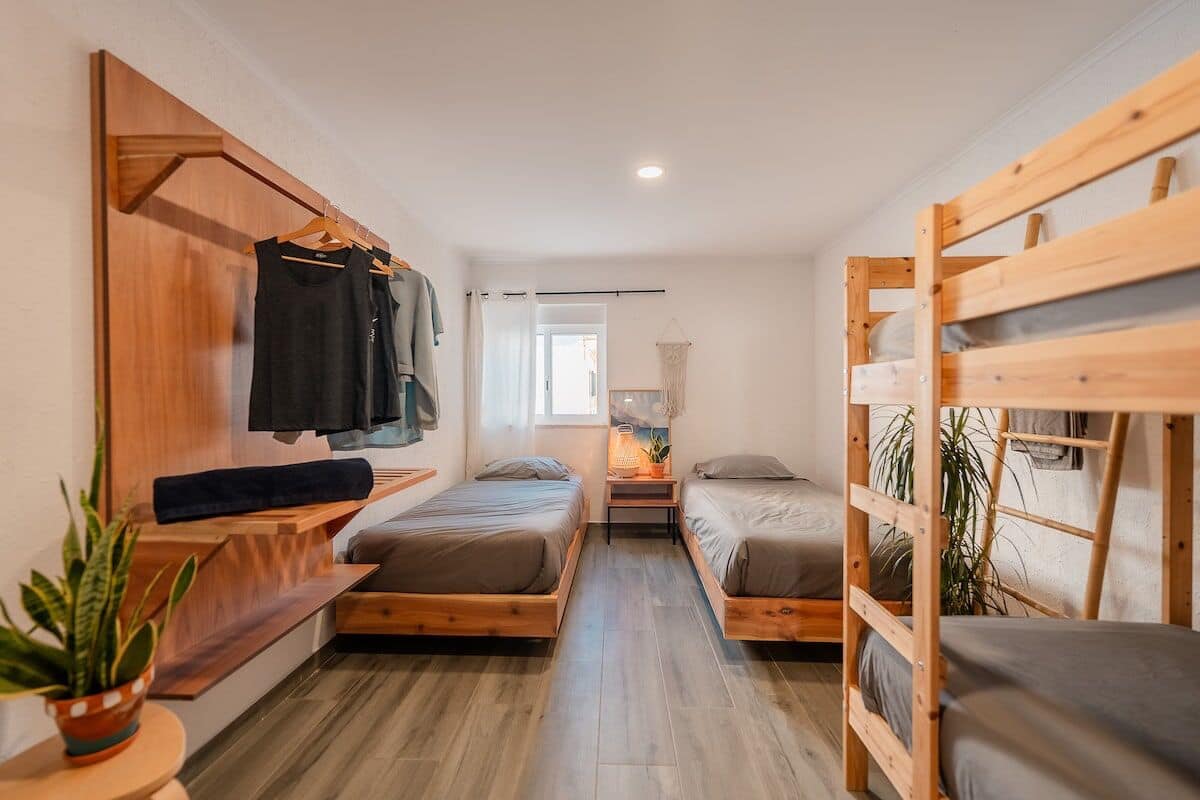 A compact room with two wooden bunk beds, a small table with a plant, and a wall-mounted clothing rack.
