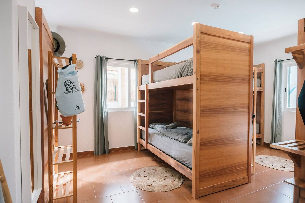 A compact room with a wooden bunk bed, a small desk, and a window with curtains.