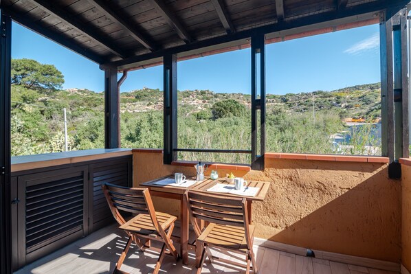 A covered outdoor seating area with a table and chairs, overlooking a hilly landscape.