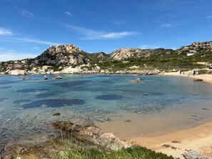 A coastal beach with clear water, rocky formations, and a distant mountain. - Studio Apartment 'Monolocale La Maddalena' with Mountain View, Wi-Fi and Air Conditioning (La Maddalena)