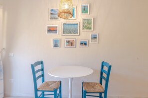 Ein Zimmer mit einem weißen runden Tisch und zwei blauen Stühlen, einer Wand mit gerahmten Bildern und einer Pendelleuchte.