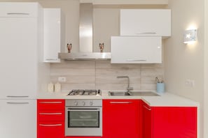 A modern kitchen with white and red cabinetry, a gas stove, a built-in oven, and a stainless steel sink. - Studio Apartment 'Monolocale La Maddalena' with Mountain View, Wi-Fi and Air Conditioning (La Maddalena)