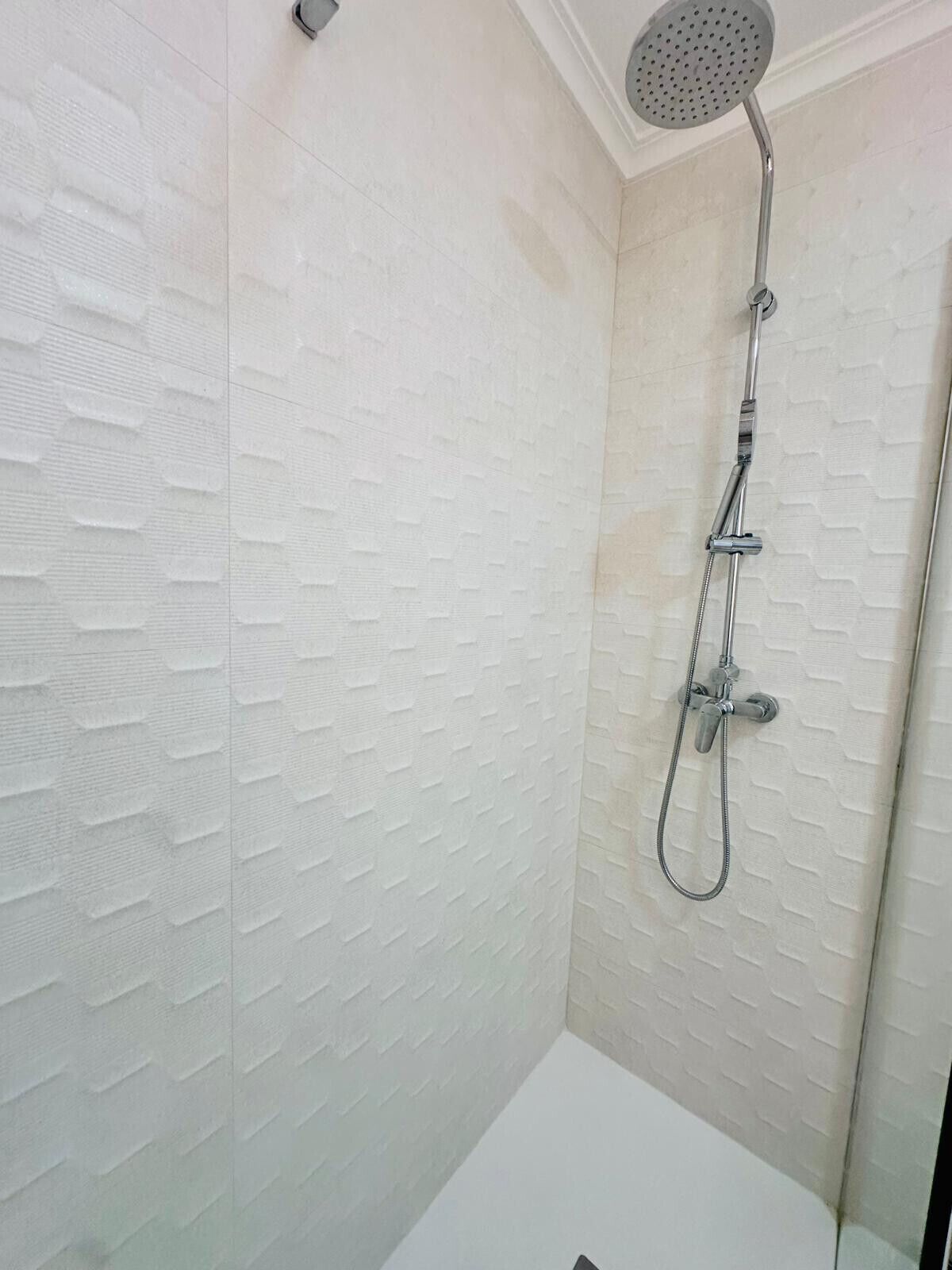 Una ducha con cabezal de ducha manual y grifo empotrado en la pared.