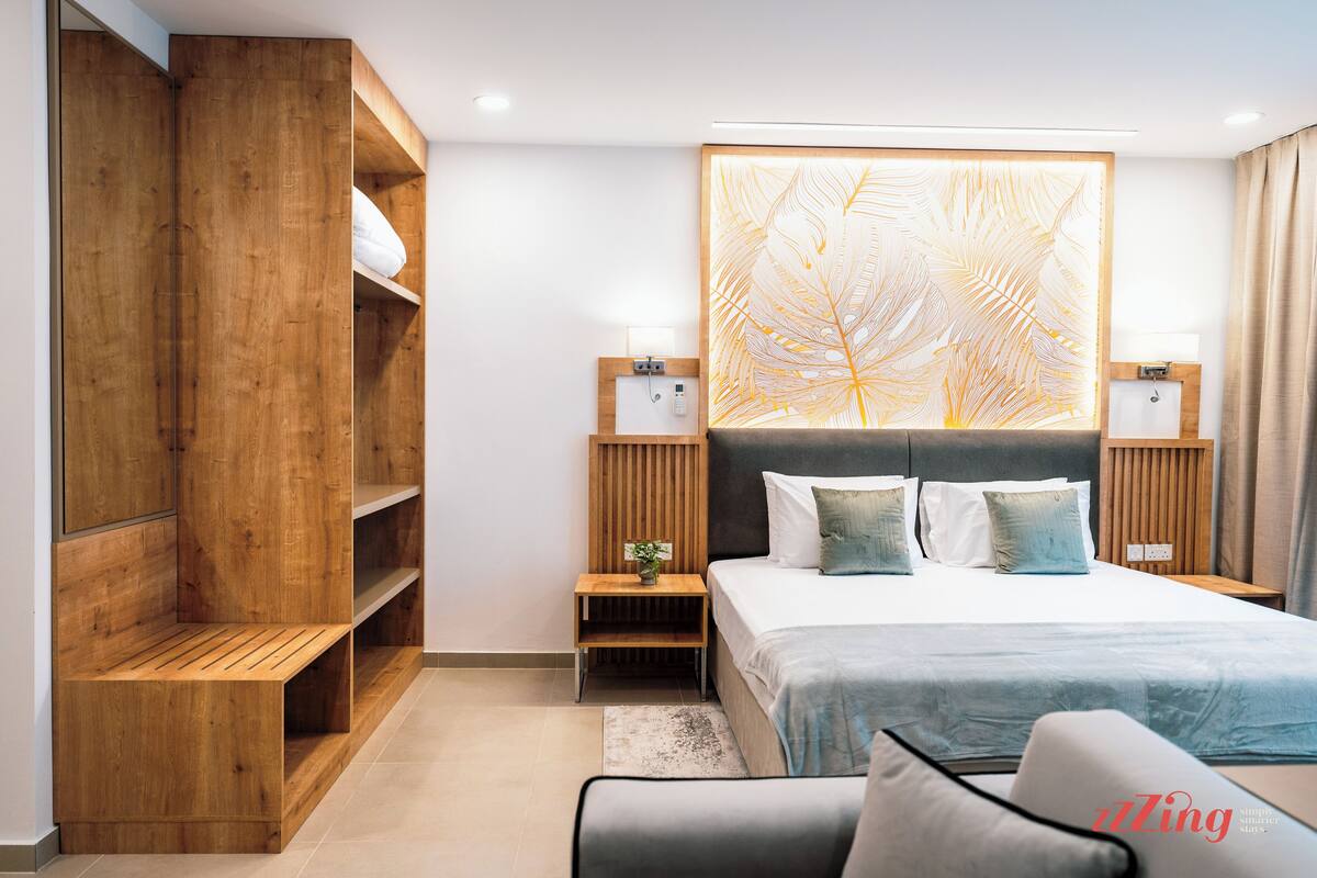 Une chambre moderne avec un grand lit, des étagères en bois, une décoration murale représentant des feuilles et une table de chevet avec une lampe.