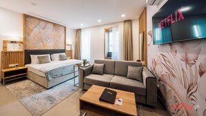 A modern hotel room with a bed, sofa, and a coffee table. A large TV screen displays the Netflix logo. - El Doris Boutique Living St Julians  (St. Julian's)