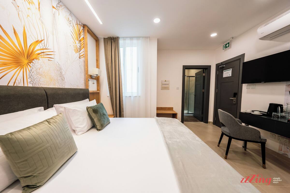Une chambre d’hôtel comprenant un lit, un bureau, une chaise, un mur orné d’un motif floral et une porte.