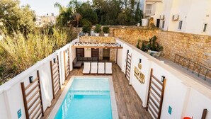 A rooftop pool area with a stone wall, wooden deck, and a seating area with cushions. - El Doris Boutique Living St Julians  (St. Julian's)