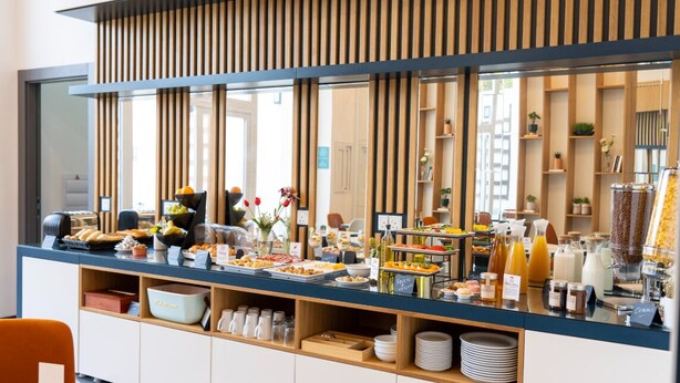 A buffet area with various food items and beverages, a seating area with chairs, and a counter with a wooden slat design. - El Doris Boutique Living St Julians  (St. Julian's)