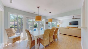 A dining area with wicker chairs, a white table, and pendant lights. - Coastal Luxe Lagoon with Pool Near Beach (Hilton Head Island)