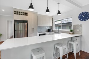 Une cuisine moderne dotée d’un grand îlot central, d’appareils électroménagers en acier inoxydable et de luminaires suspendus.