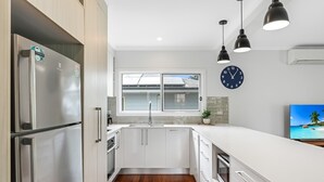 Une cuisine moderne dotée d’appareils électroménagers en acier inoxydable, de meubles blancs, d’un plancher en bois et d’un éclairage suspendu.