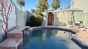 A swimming pool with steps leading into it, surrounded by a wall with a tree mural, palm trees, and a small building with a door. - DOWNTOWN PHX PRIVATE BEDROOM SHARED BATHROOM KITCHEN COMMON AREAS SWIMMING POOL (Phoenix)