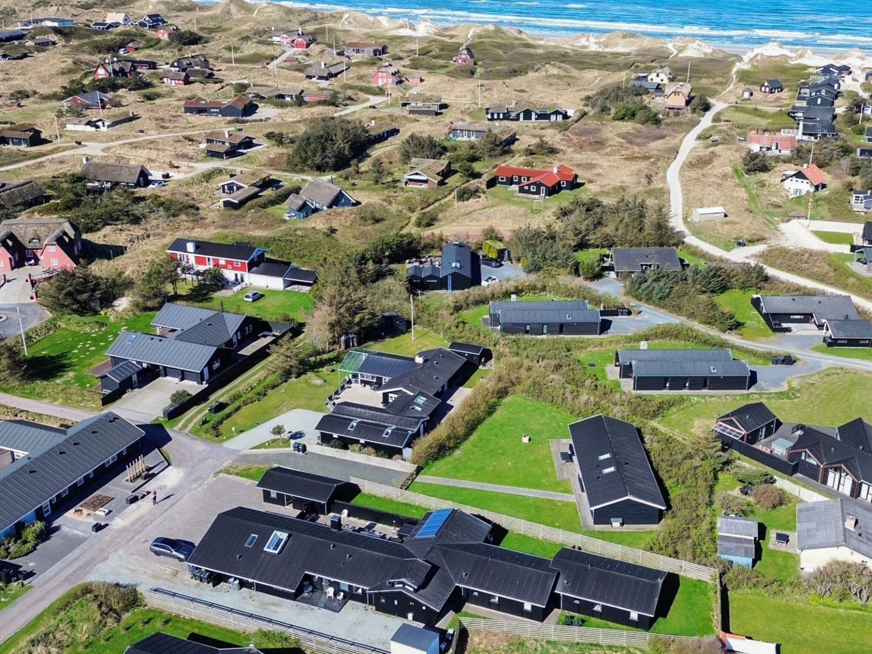 An aerial view of a coastal residential area with houses, roads, and a beach in the background.