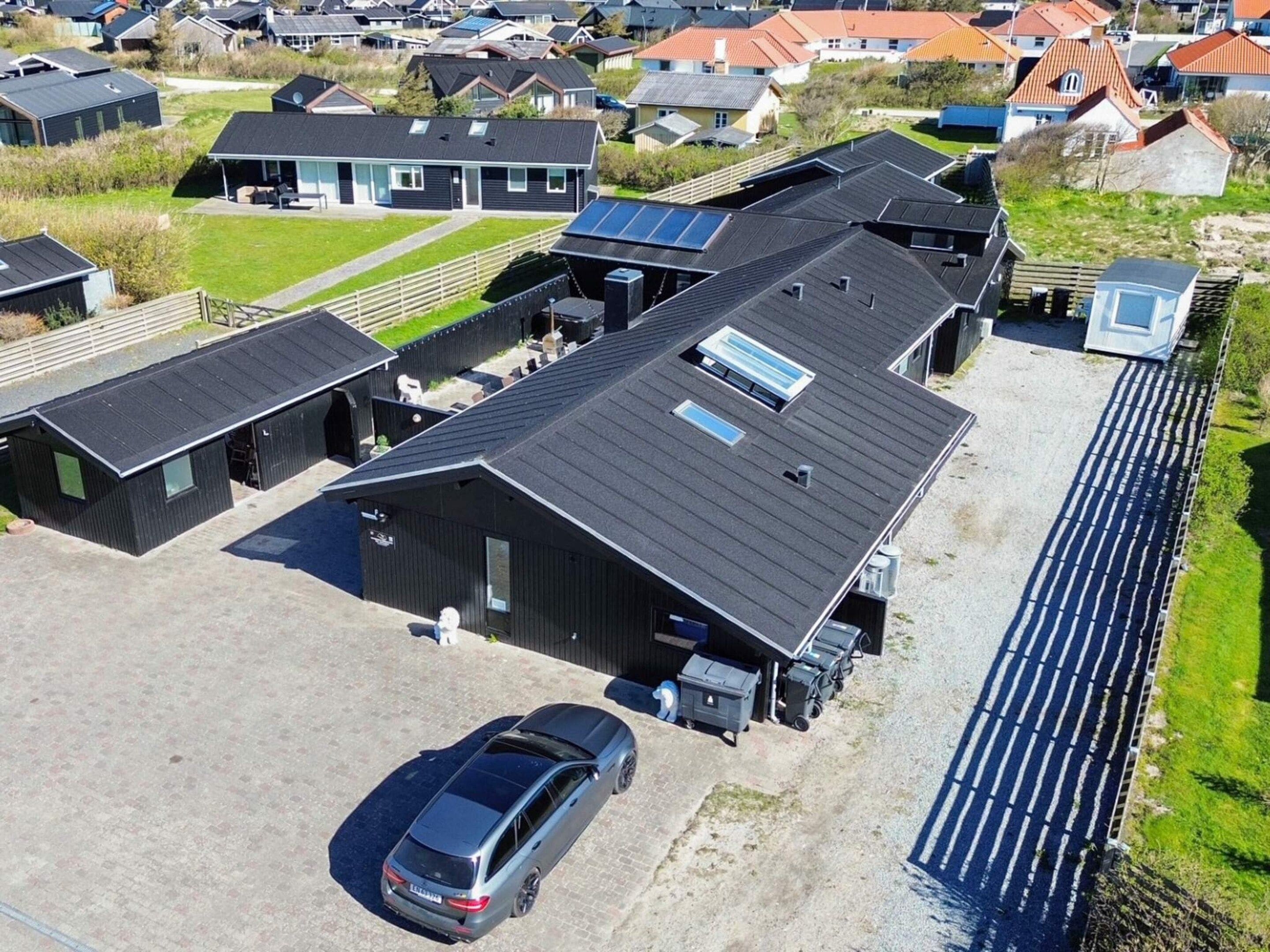 Ett flygbildsbild av ett bostadsområde med flera hus, en stor byggnad med ett sluttande tak och en parkerad bil.