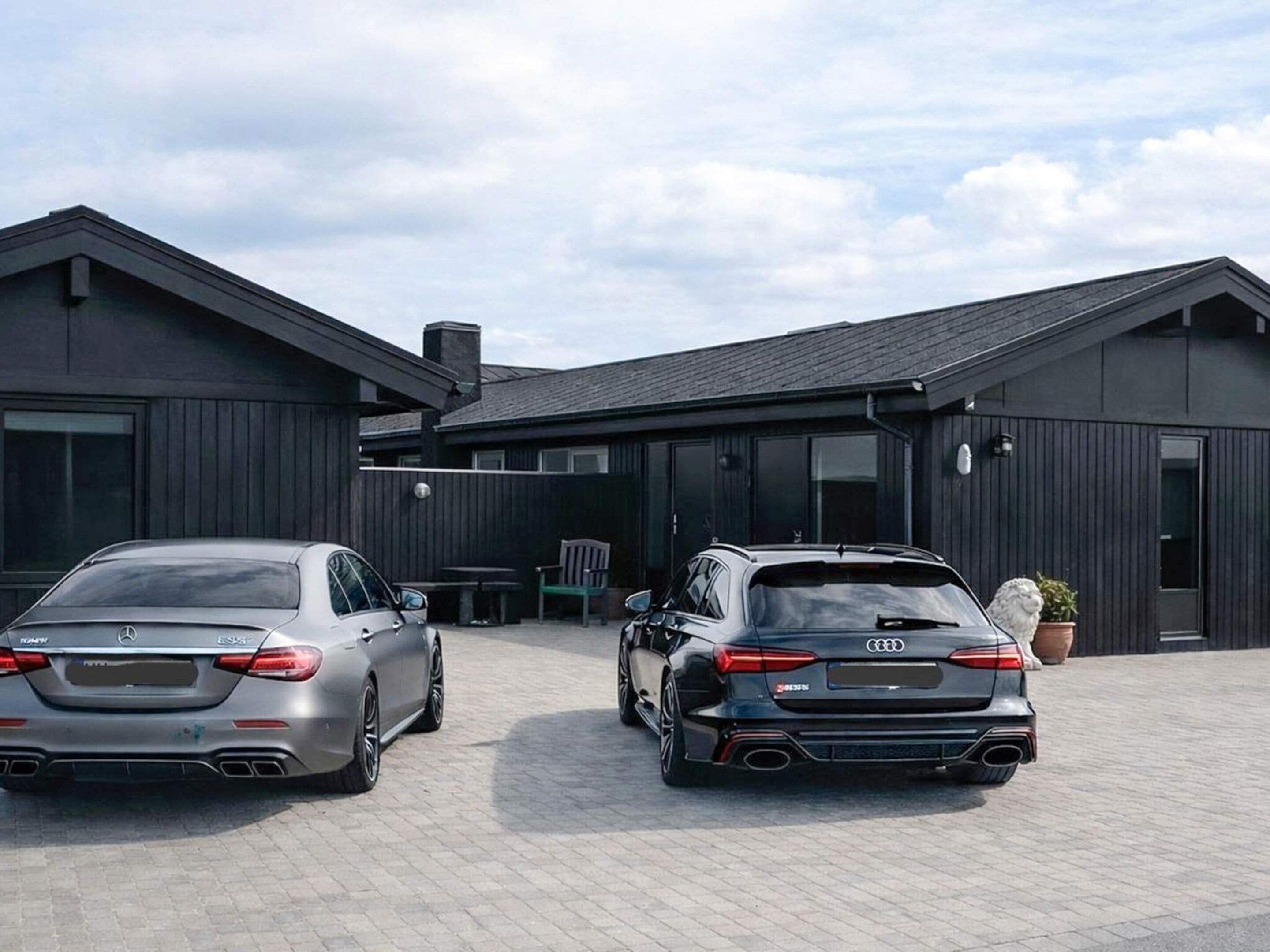 Two luxury cars parked in front of a modern building with a paved driveway.