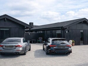 Two luxury cars parked in front of a modern building with a paved driveway. - 4 Star Holiday Home in Blokhus (Blokhus)