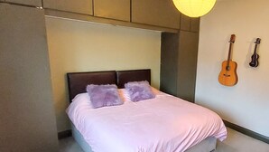 Ein Schlafzimmer mit einem Bett, zwei Gitarren an der Wand und einer Hängelampe.