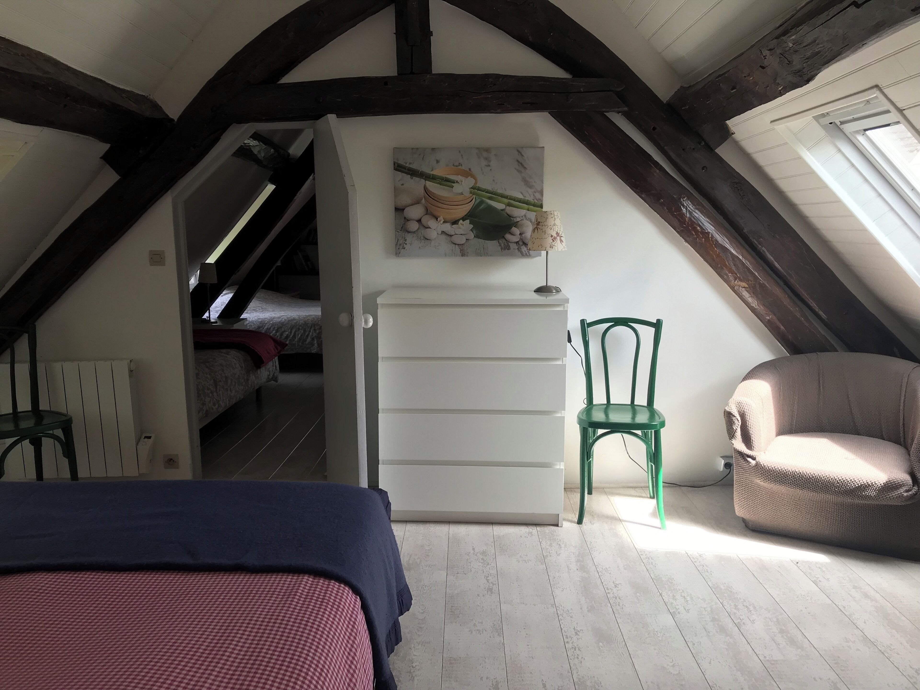 Een slaapkamer met een schuine kap, een bed, een stoel, een dressoir en een schilderij.