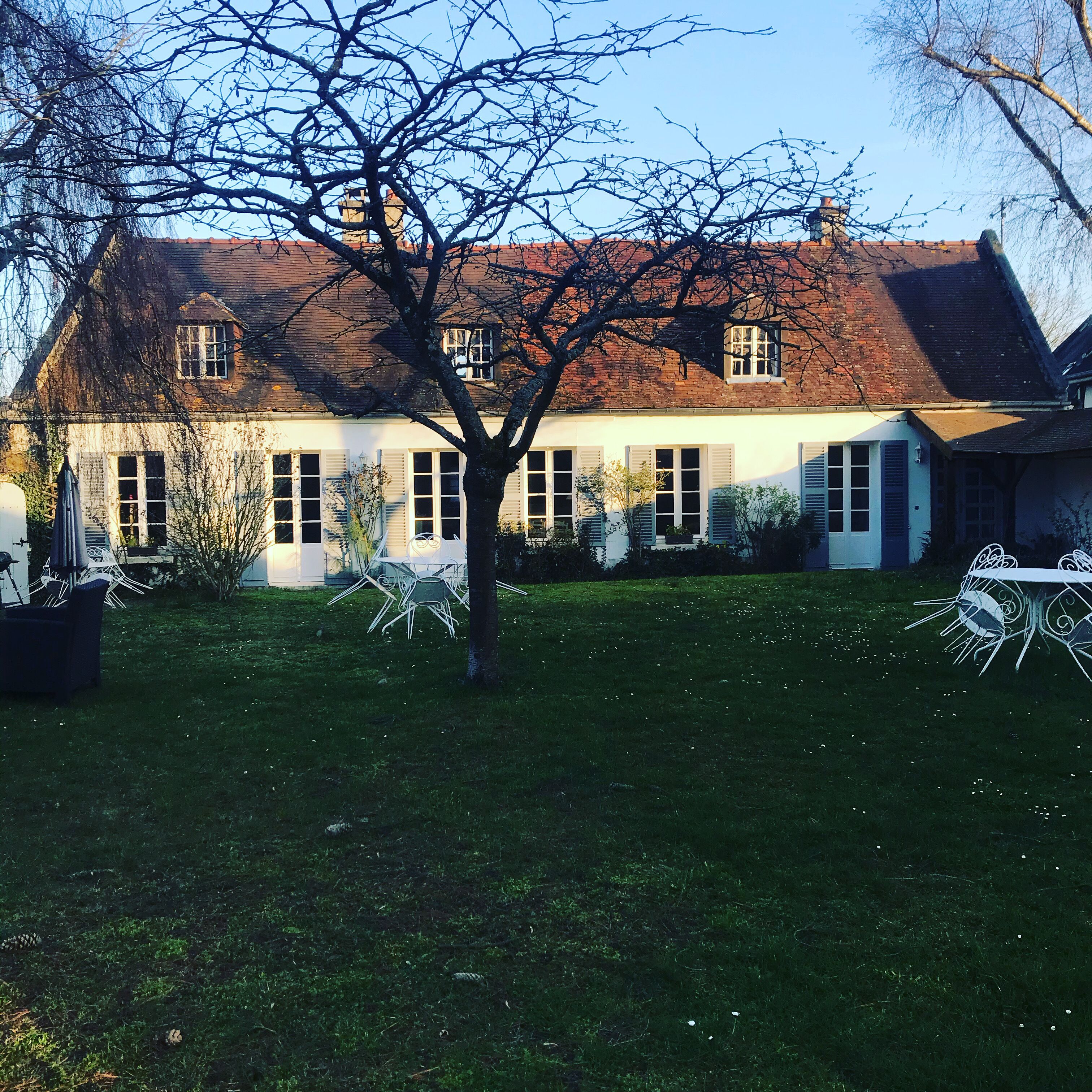 Een traditioneel huis met een dak van baksteen, witte luiken en een verzorgd gazon.