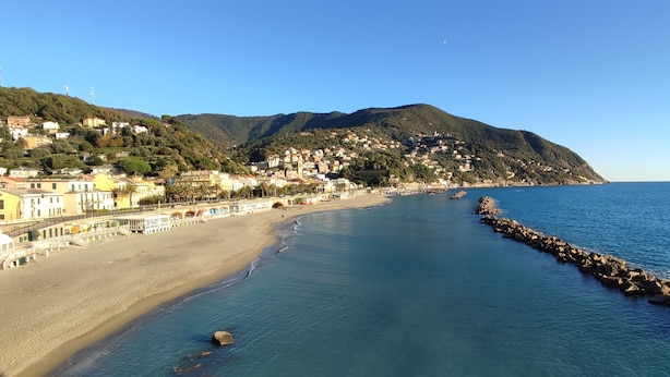 Uma cidade costeira com praia, casas e montanhas ao fundo.