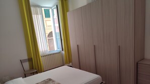 Quarto com cama, radiador, janela com cortinas e guarda-roupa.