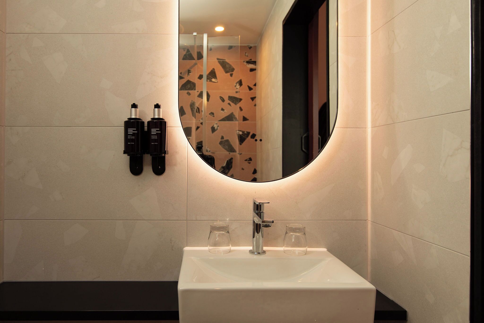 Ein Badezimmer mit einem weißen Waschbecken, einem Spiegel und zwei Flaschen an der Wand.