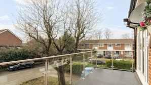 A residential balcony with a glass railing, a satellite dish, and a view of a street with parked cars and houses. - Close to Windsor, Heathrow and central London — sleeps nine (Berkshire)