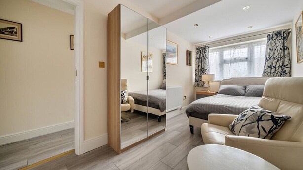 A modern bedroom with a large mirror, a bed, a sofa, and a nightstand. - Close to Windsor, Heathrow and central London — sleeps nine (Berkshire)
