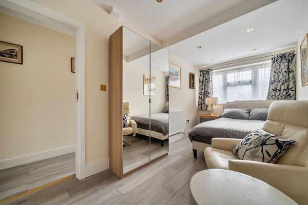 Bedroom showing a full-height mirrored sliding wardrobe, a cream leather sofa chair with patterned cushions, and a small round side table.