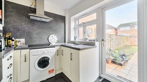 A compact kitchen with a washing machine, a built-in oven, and a window overlooking a backyard. - Close to Windsor, Heathrow and central London — sleeps nine (Berkshire)