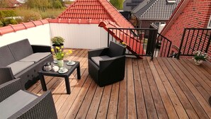 A wooden deck with outdoor furniture, a staircase, and a red-tiled roof. - Cozy vacation apartment "Lütje Moew", 4-room with roof terrace, rural location (Leezdorf)