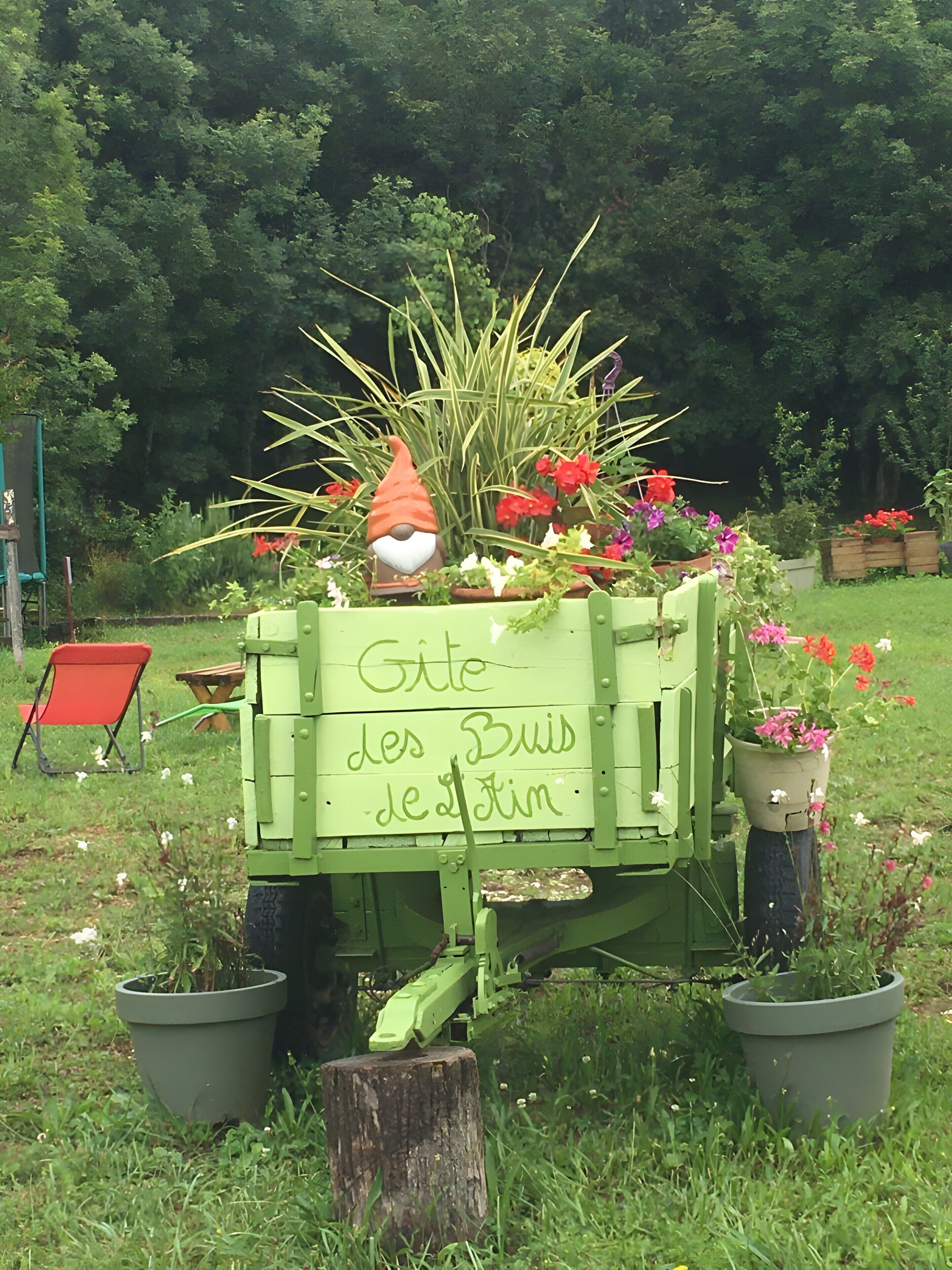 A green garden cart with a gnome figure and potted plants.