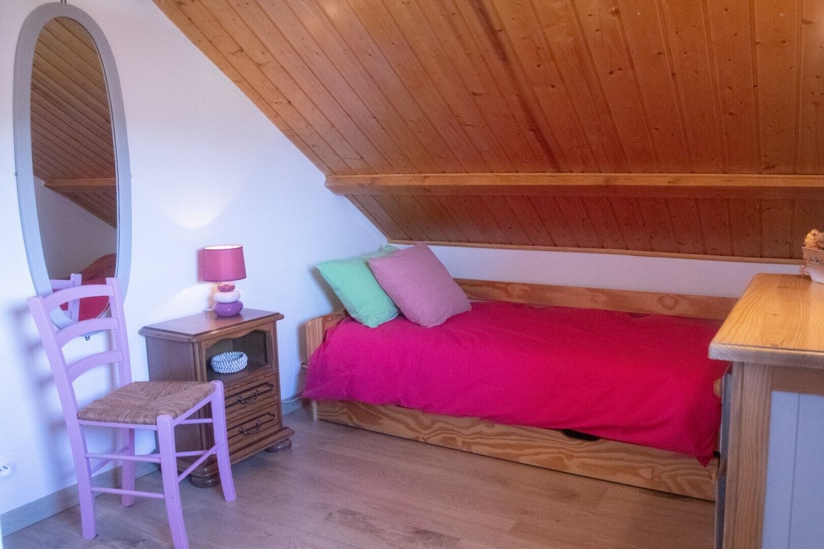 Un dormitorio con techo inclinado, una cama de madera, una silla, una mesita de noche y un espejo.