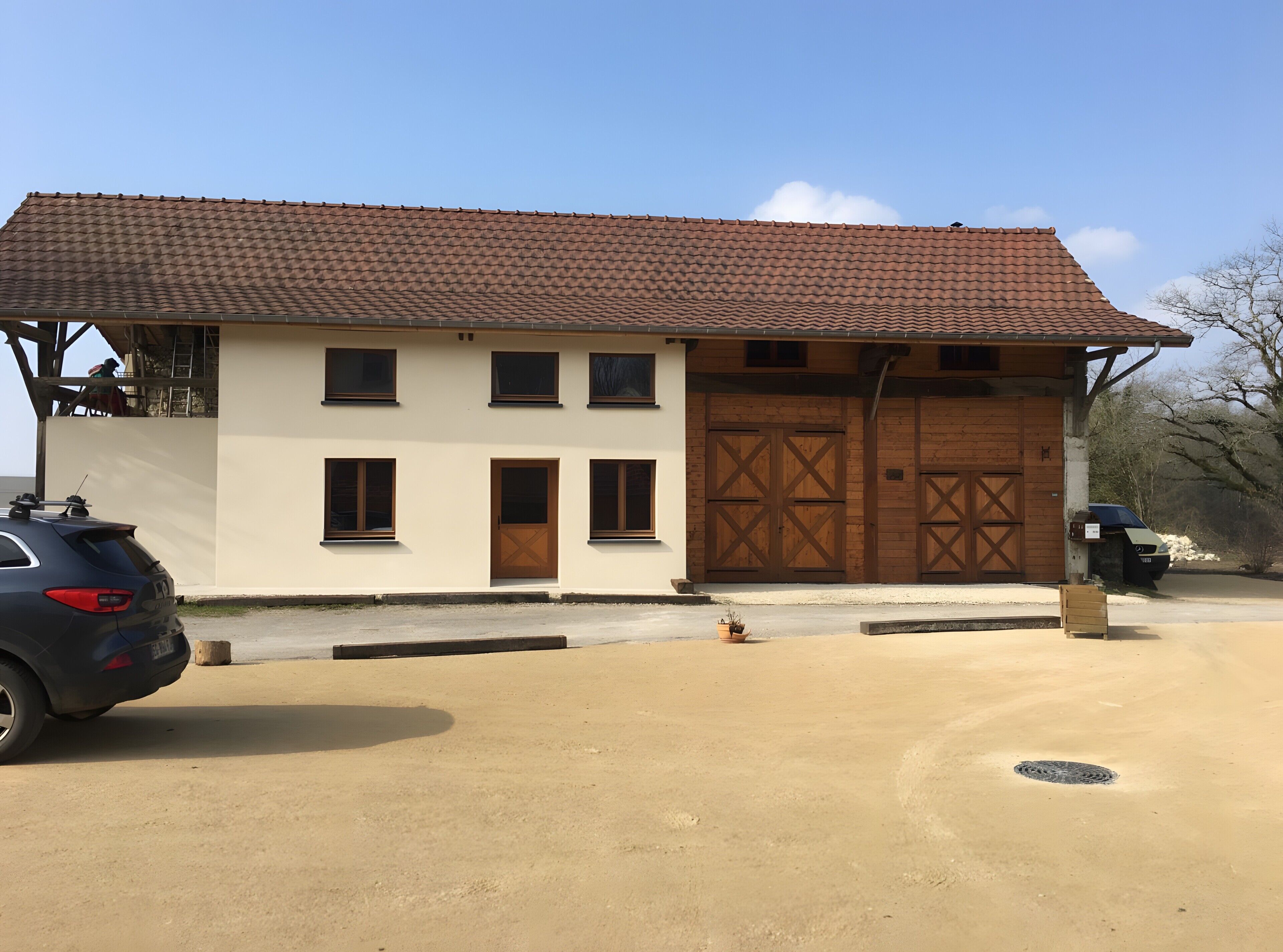 A two-story building with a tiled roof, a garage with wooden doors, and a parked car in the foreground.