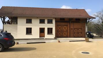A two-story building with a tiled roof, a garage with wooden doors, and a parked car in the foreground.