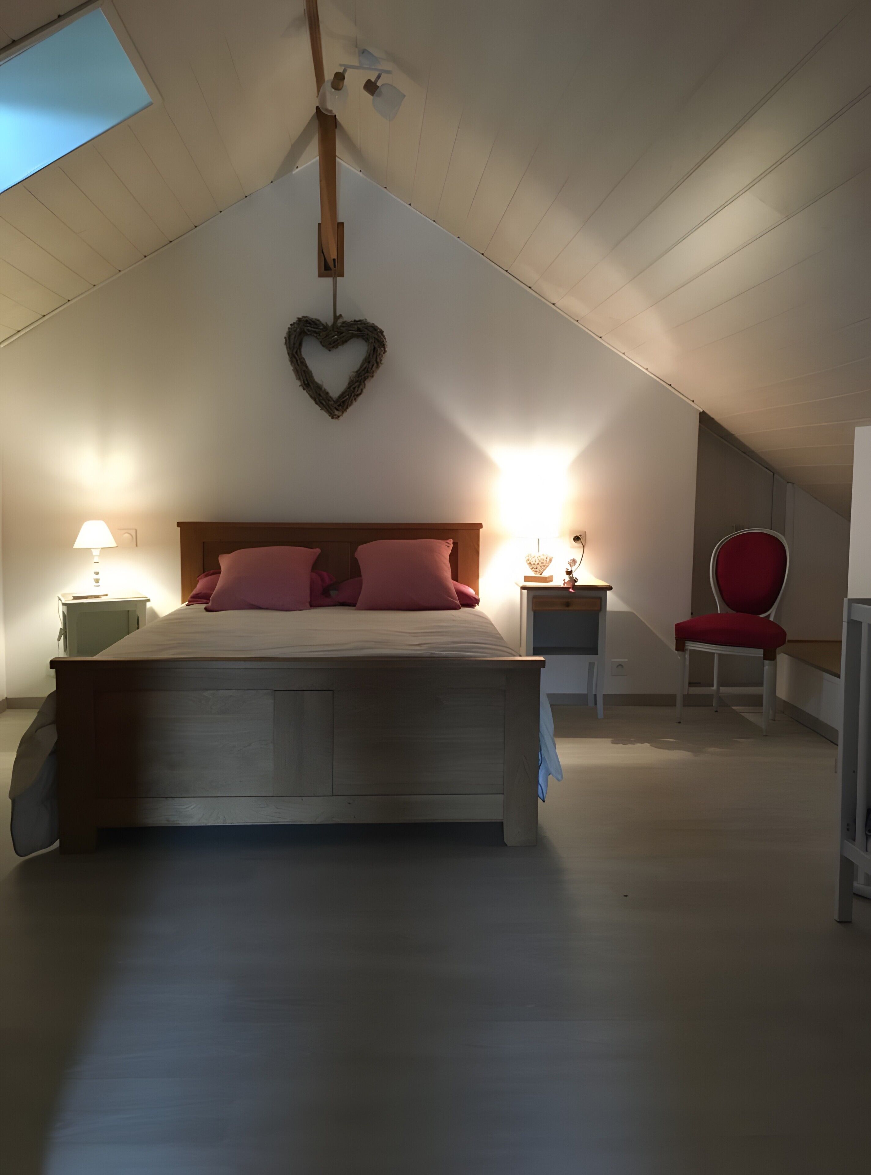 Una camera da letto con un letto di legno, una decorazione a forma di cuore, una sedia rossa e due lampade da comodino.