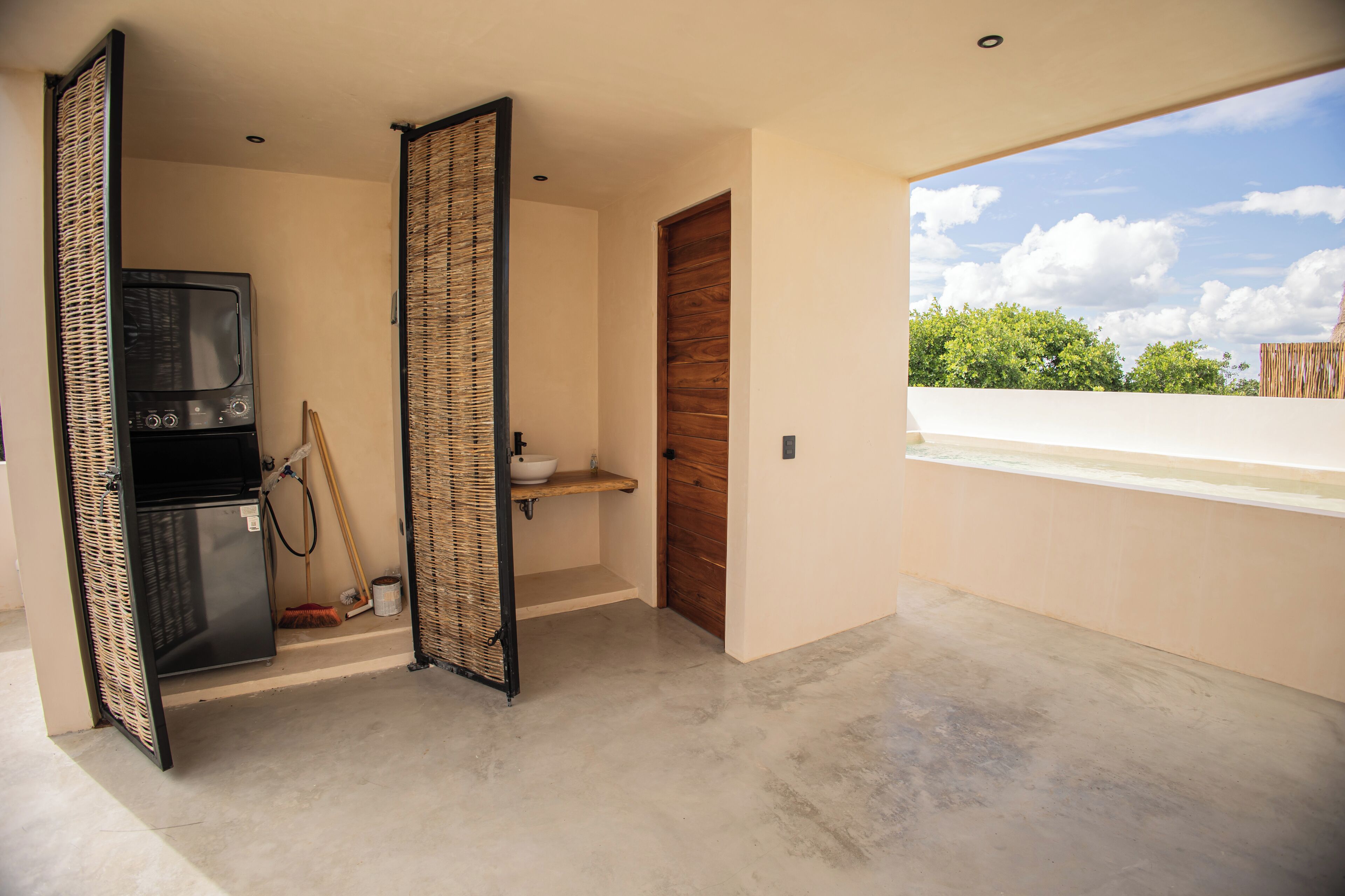 Un intérieur moderne avec une kitchenette, une porte en bois et un balcon offrant une vue sur les arbres.