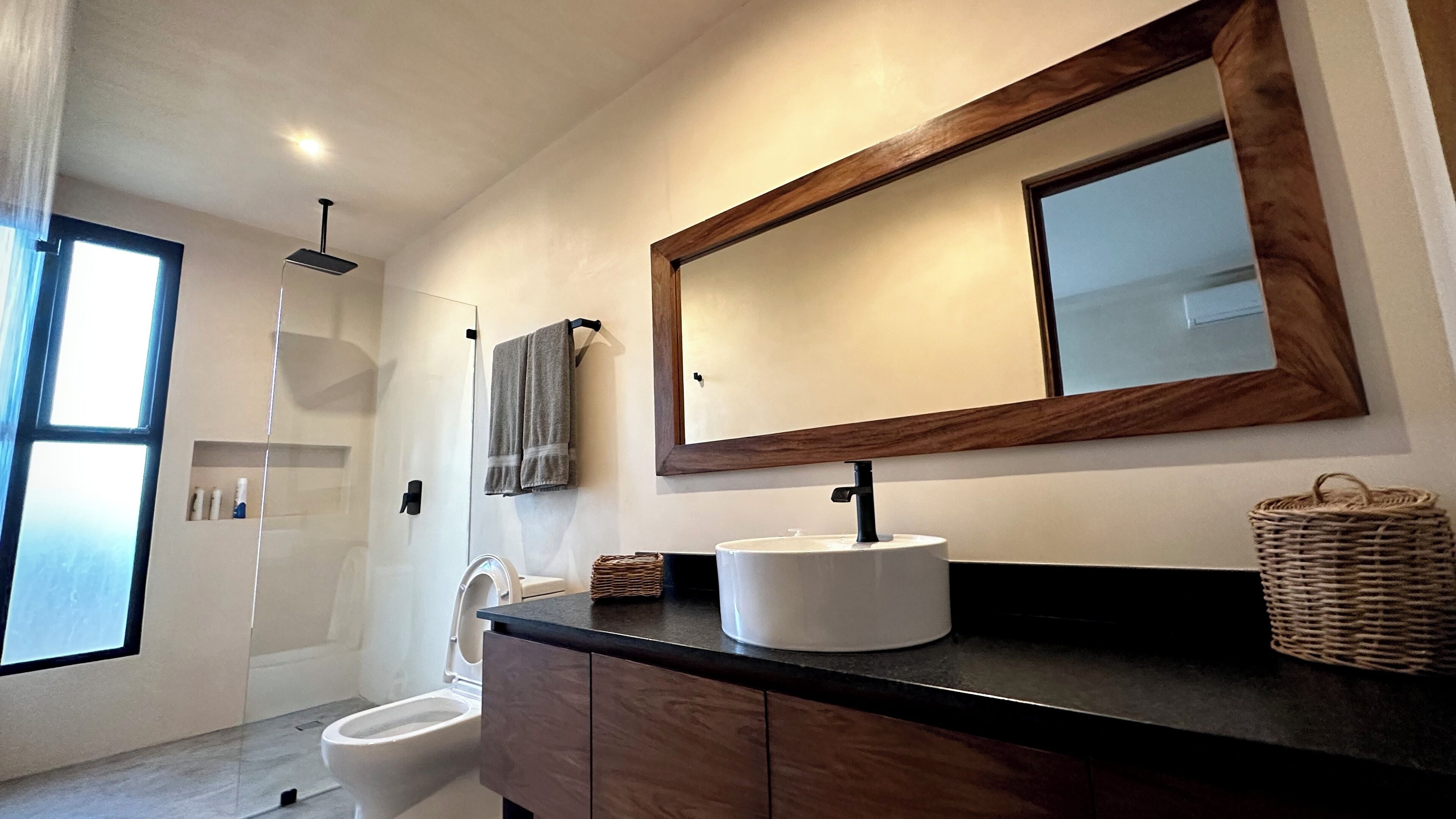 A modern bathroom with a large mirror, a white sink, and a shower.